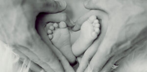 two pairs of adult hands surround a pair of baby's feet in a heart shape